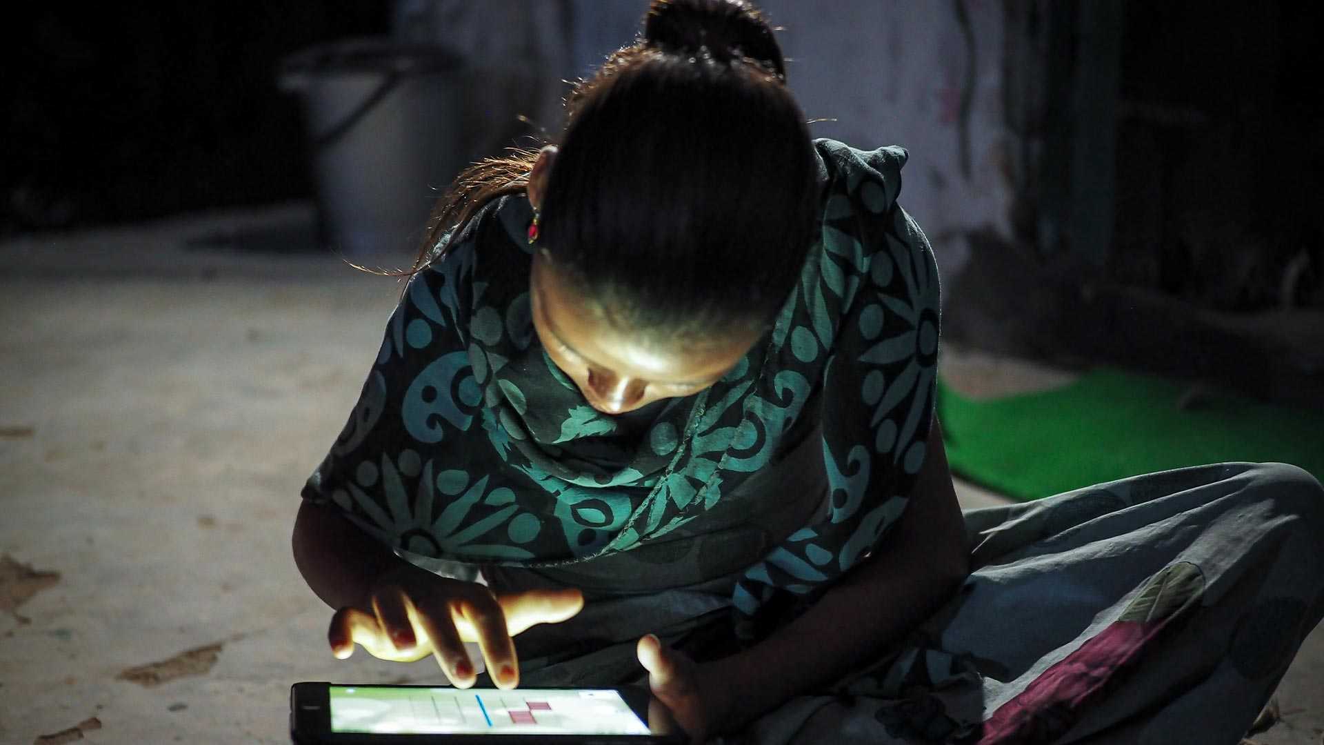 A young girl in India studying on a tablet at night